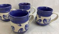 Four ceramic mugs with blue floral designs and deep blue rims arranged together.