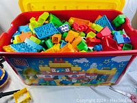 Red plastic box filled with assorted large Mega Bloks including multiple colors such as yellow, orange, green, blue, and red.