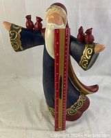 Full view of ceramic Santa figurine with arms outstretched holding four small birds, holding a ruler for scale.