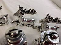 Four shiny silver-tone metal reindeer figurines lying down, used as place card holders for Christmas table decor.