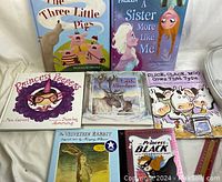 Various children's books displayed on a white surface, showing 7 different titles including The Three Little Pigs and Frozen: A Sister More Like Me.