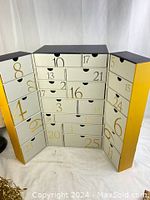 Front view of the open advent calendar showing 25 numbered compartments in the center and side panels with various sized drawers.