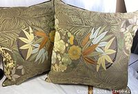 Photo of two large throw pillows side by side showing brown and gold plant design pattern with leaves and flowers.