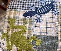 Close-up of the comforter showing blue and green lizard appliqué details on patchwork plaid fabric.
