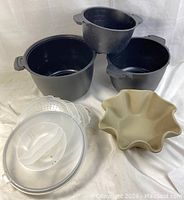 All black plastic microwave steamer pieces and ceramic wavy bowl arranged together showing sizes and lids.