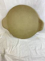 Top view of light beige oval Pampered Chef pizza stone showing entire surface and two handles.