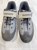 Front view of pair of gray and black Shimano biking shoes showing laces and Velcro strap with brand name