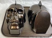 Two-piece skull shaped cake baking pan showing the detailed face front half and the back half pan.