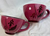 Two purple Starbucks mugs with black floral design on exterior, showing front and side view
