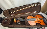 Full-size Stentnor violin in hard case with bow, violin rest, tuner, and rosin visible.