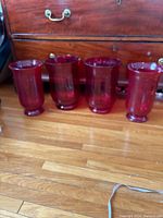 Front view showing four red glass vases arranged in a row, two smaller and two larger urn-shaped ones