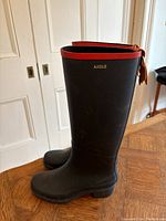 Side profile of two black Aigle Miss Juliet rubber riding style rain boots with red leather trim and pull tab, size 7 slim