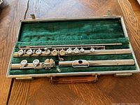 Complete flute in original case showing three parts: headjoint with sterling silver lip riser, body, and footjoint, lying on green velvet lining.