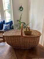 Front view of large vintage French double sided picnic basket with handle and the smaller miniature picnic basket resting on top