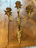 Full view of gold metal 3-arm vintage Hollywood Regency style wall sconce showing detailed leaf motifs and candle cups.
