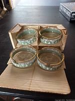 Four vintage ashtrays with green Roman Grecian band and gold trim displayed with original cardboard holder