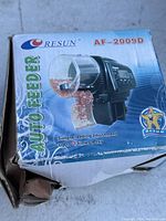 Front view of the auto feeder box showing the product name Resun AF-2009D with image of the feeder and text about feeding adjustment