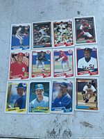 Photo of 12 baseball cards laid out on ground showing players in pitching and catching poses, various teams and brands Topps and Fleer.