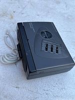 Side angle view of the black personal cassette player showing volume control and attached cord.