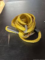 Full view of coiled yellow nylon rope with metal anchor weight and protective end coverings