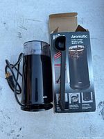 Photo showing the black Braun Aromatic coffee grinder with transparent lid, power cord, and original box.