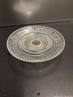 Clear crystal glass plate with detailed pattern and scalloped edge shown on dark background, photo 1.