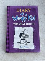 Front cover of Diary of a Wimpy Kid The Ugly Truth hardcover book, purple cover with title text and cartoon illustration.