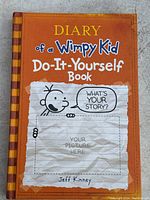 Front cover of the Diary of a Wimpy Kid Do-It-Yourself Book showing title, author, and a cartoon character with space for a picture.