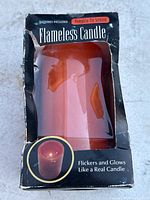 Front view of boxed flameless candle showing orange candle inside window packaging with text.
