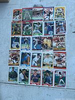 Photo showing a collection of 24 football and baseball trading cards arranged on a flat surface with various players and teams represented.