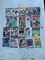 Top-down view of the full lot of 20 football cards laid out in a grid on a concrete surface, showing various NFL players mostly in action shots from the 1990s Pro Set series.