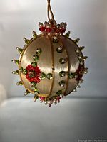 Full view of the handmade Christmas ornament showing satin fabric sections with gold trim, bead decorations, and red flower appliques.