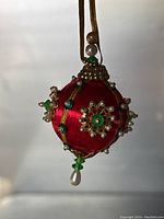 Front view of the handmade red satin Christmas ornament with green rhinestones, pearl beads, and gold accents