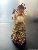 Front view of vintage burlap and cardboard angel tree topper with gold tinsel skirt, white and gold wings and candle details.