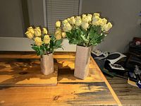 Two rectangular vases with lifelike artificial cream yellow rose stems placed on a wooden table.