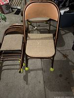 Front view of one chair showing the vinyl backrest, cushioned seat with beige patterned fabric, and tennis ball caps on metal legs.