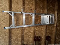 Photo showing a 5-foot aluminum step ladder with four steps, including top platform and rubber feet caps, leaning against wooden wall