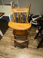 Front view of the antique child's highchair showing tray, seat and legs on wooden flooring