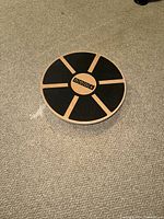 Top view of wooden circular balance board showing six black grip lines and central Vigour logo on top surface.