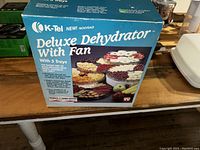 Box of K-Tel Deluxe Food Dehydrator showing product details and images of trays with dried fruits.