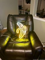Neon banana sign illuminated on a brown leather recliner chair showing the yellow and white neon lighting effect.