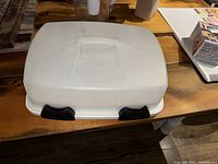 White plastic cake and mini muffin holder server with lid and two black latches on the sides, closed and viewed from top and side angles.