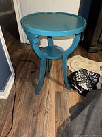 Side view of the blue round side table showing the curved legs and lower shelf.