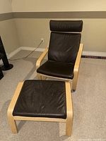 Front view of Ikea rocker chair with matching stool on carpeted floor showing light wood frame and black leather cushions.
