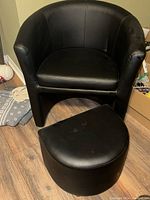 Photo of black faux leather chair with matching rounded stool on wooden floor.