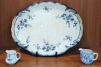 Photo showing the oval floral serving platter flanked by two small creamers on a wooden surface