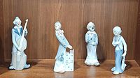 Four vintage Casades porcelain clown figurines displayed on wooden shelf: double bass clown, dice clown, blue nose clown, saxophone clown.