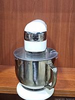 Front view of the white Cuisinart Precision mixer with stainless steel bowl and splash guard, placed on wooden surface.