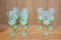 Seven green depression glass stemmed wine glasses arranged in two rows against a wood background, showing their full shape and flared rims