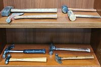 Shows assortment of 8 used hammers with wooden and metal handles, various types arranged on a shelf.